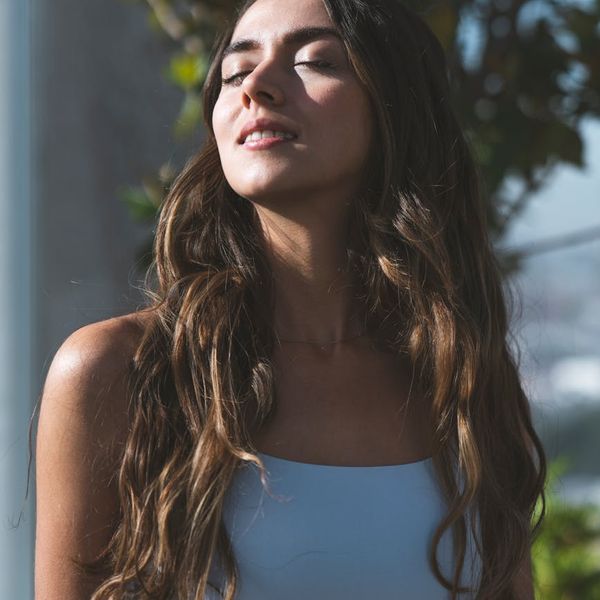 Woman smiling peacefully during a yoga session, sunlight in background.